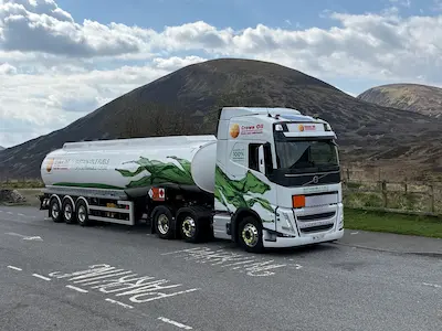A Crown Oil branded articulated tanker in front of a hill